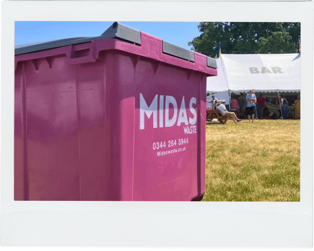A close-up image of a pink Midas Waste wheelie bin in front of some food stalls at a festival event in Kent
